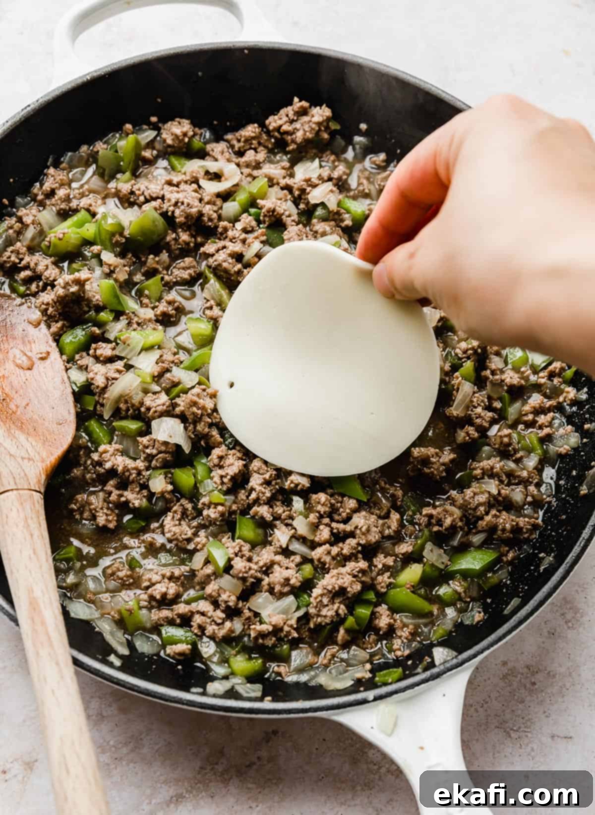 Φιλαδέλφειας Τυρόστεικ Σλόπι Τζο 6 A hand placing a slice of provolone cheese on top of Philly Cheesesteak Sloppy Joes mixture in a skillet.
