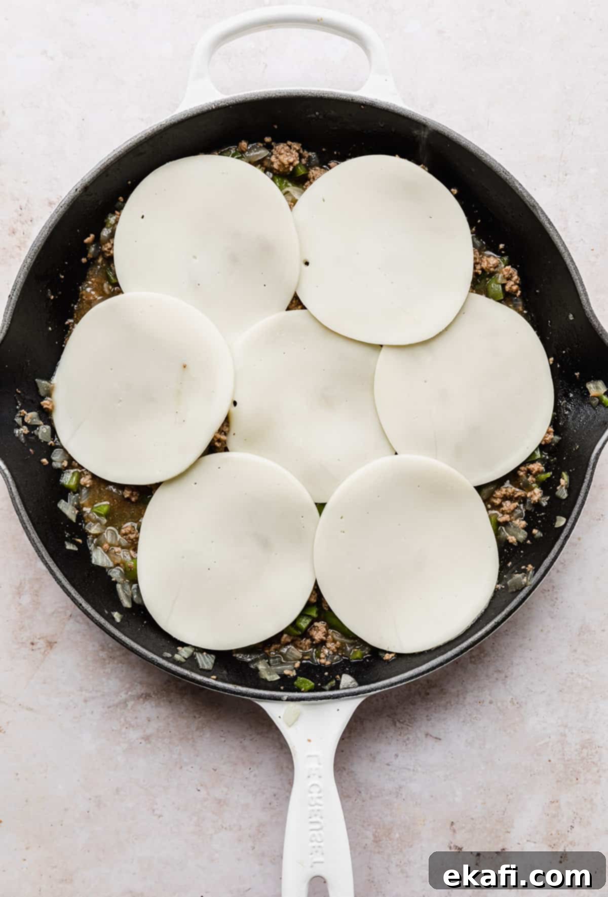 Φιλαδέλφειας Τυρόστεικ Σλόπι Τζο 7 Provolone cheese topped Philly Cheesesteak Sloppy Joes mixture in a white skillet.