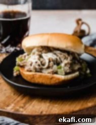 Φιλαδέλφειας Τυρόστεικ Σλόπι Τζο 10 A Philly Cheesesteak Sloppy Joe on a black plate with a clear glass full of brown liquid in the background.