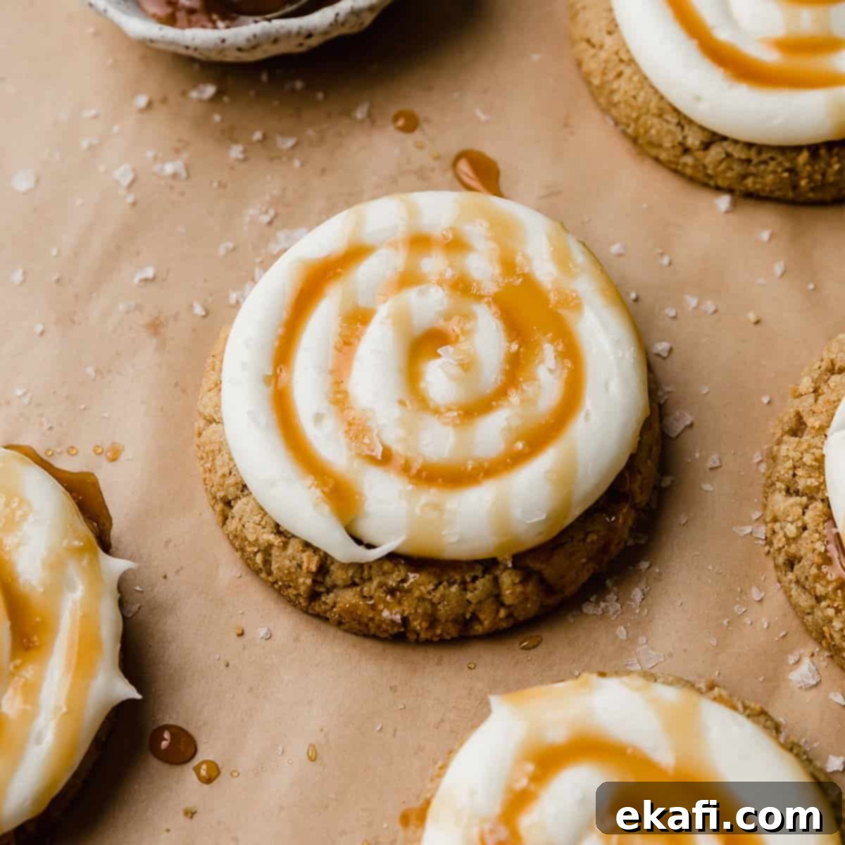 Ένα Salted Caramel Cheesecake Cookie σε μπεζ αντικολλητικό χαρτί, το μπισκότο καλύπτεται με καραμέλα και λευκό γλάσο.