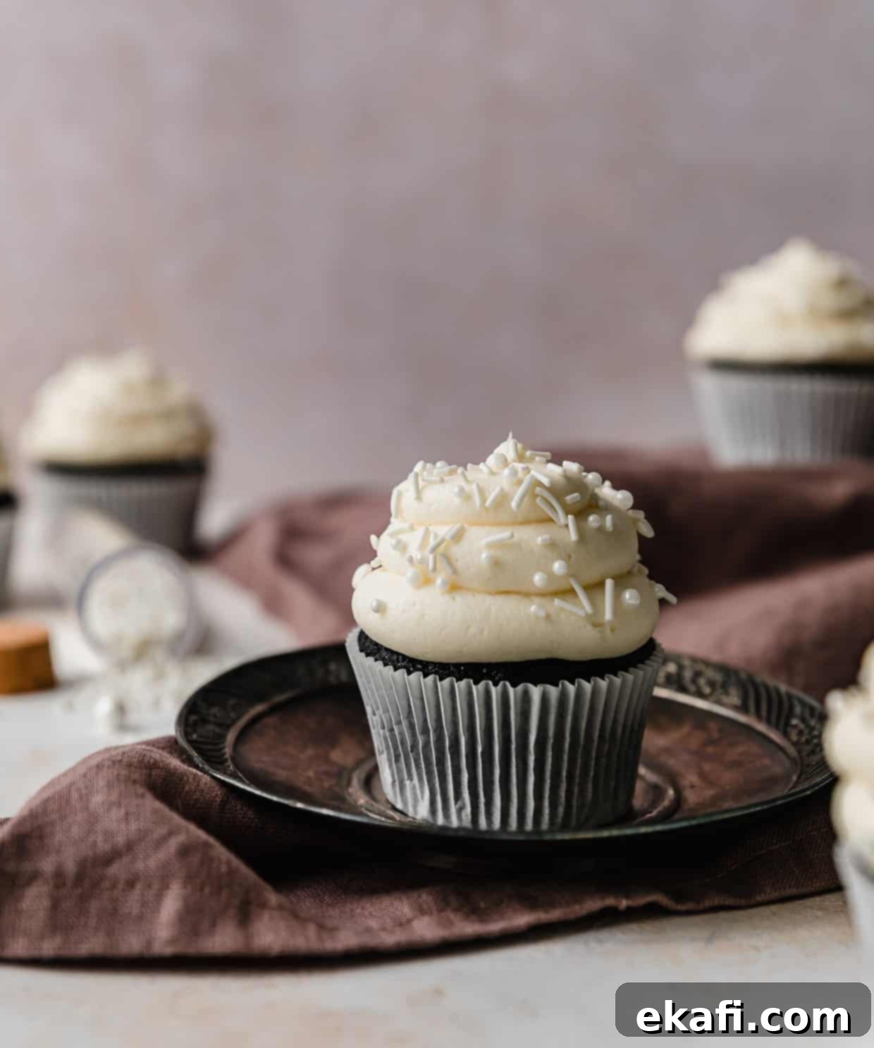 Επικάλυψη Σαντιγί 5 Ένα cupcake γαρνιρισμένο με μια σπείρα από γλάσο σαντιγί λευκής σοκολάτας με πουτίγκα και λευκά τρουφάκια, σε ένα ανοιχτό μοβ φόντο.