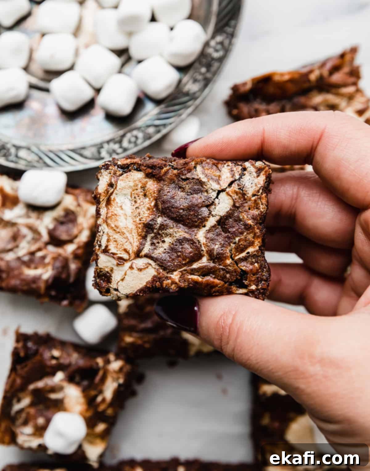 Ένα χέρι κρατά ένα τετράγωνο Marshmallow Brownie, με κρέμα marshmallow αναμεμειγμένη στην κορυφή.