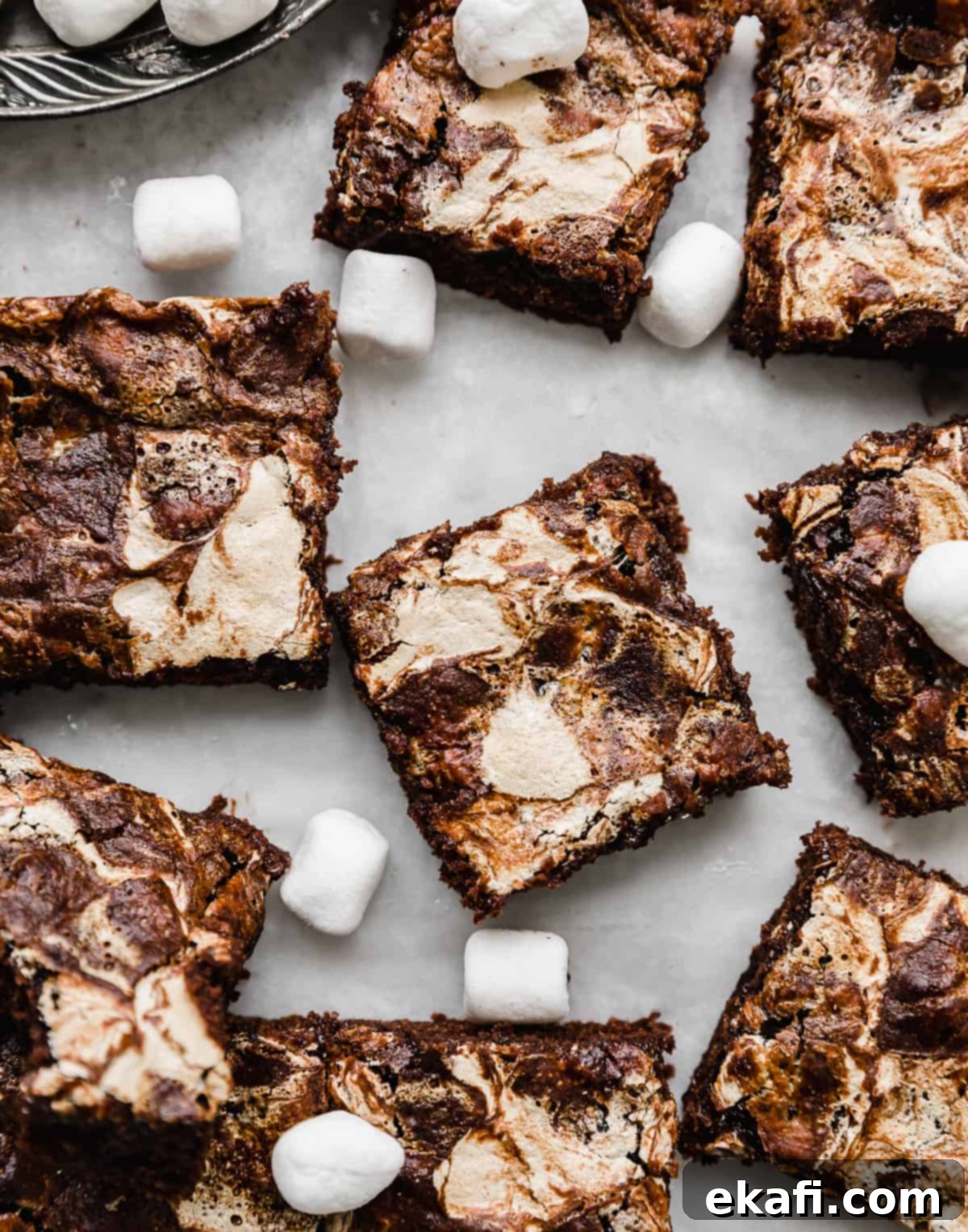 Μαρσμέλοου Μπράουνις 7 Φωτογραφία από πάνω Marshmallow Brownies κομμένα σε τετράγωνα σε λευκό λαδόκολλα με μίνι marshmallows σκορπισμένα τριγύρω.