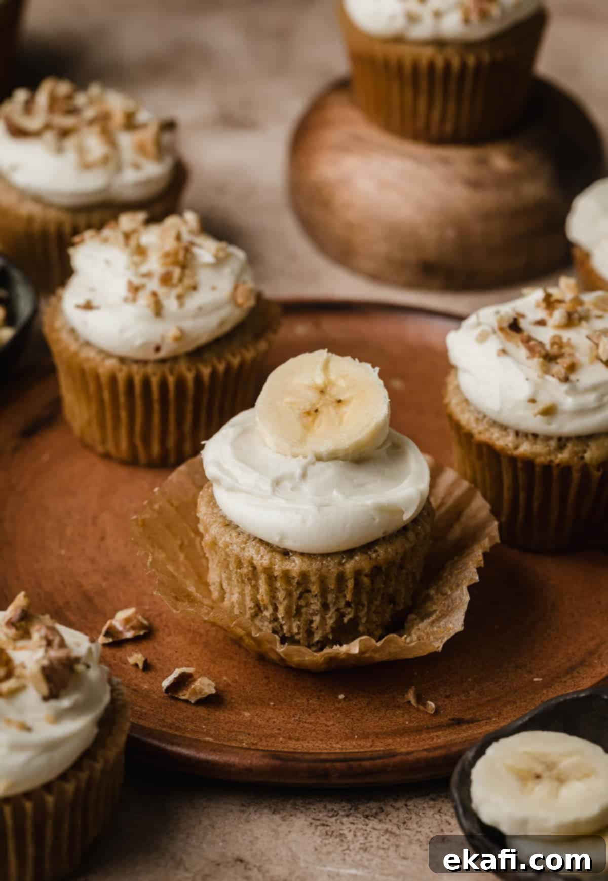 Συνταγή για Κάπκεϊκς Μπανάνας 2 Cupcakes μπανάνας με γλάσο τυριού κρέμας και φέτα μπανάνας, σε ένα καφέ πιάτο.