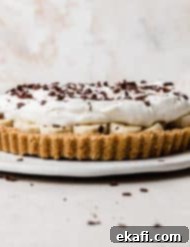 Μια Banoffee Pie σε ένα λευκό πιάτο, με σαντιγί και ξύσματα σοκολάτας στην κορυφή.