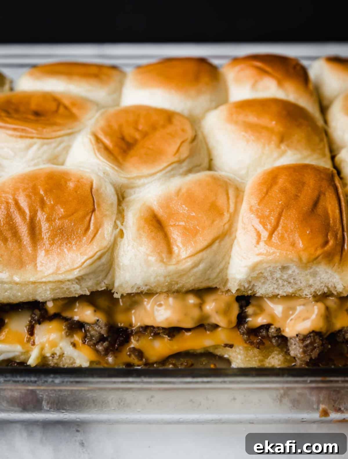 Μίνι Σάντουιτς Πρωινού 7 Ψημένα Hawaiian Roll Breakfast Sliders σε γυάλινο ταψί που δείχνουν τις στρώσεις ομελέτας, τυριού και λουκάνικου.
