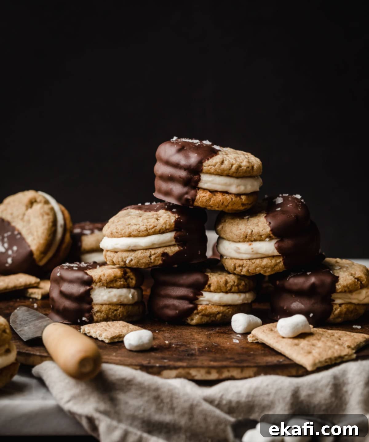 Μπισκότα Σάντουιτς Σ'μόρες 2 Μπισκότα S'mores Σάντουιτς με κρέμα μαρσμέλοου ανάμεσα σε μπισκότα graham cracker, βουτηγμένα μέχρι τη μέση σε σοκολάτα, σε μαύρο φόντο.