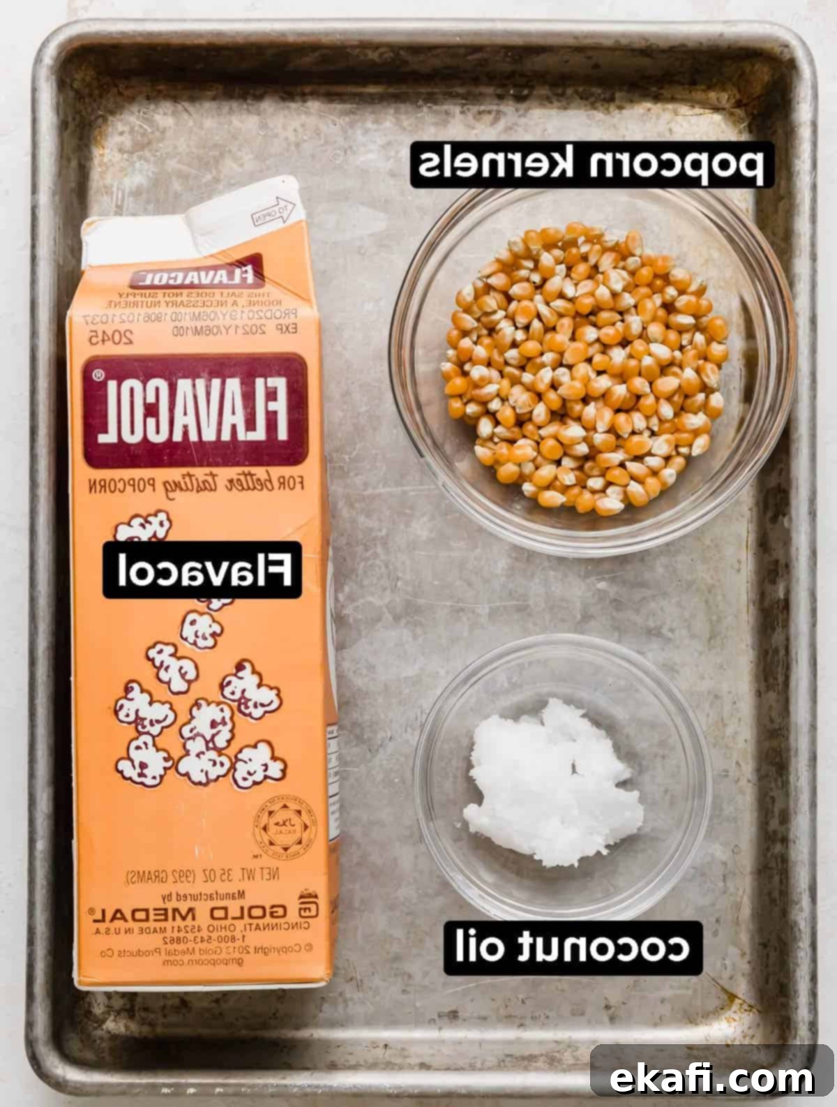 Σπόροι ποπ κορν, λάδι καρύδας και Flavacol σε ένα γκρι ταψί.