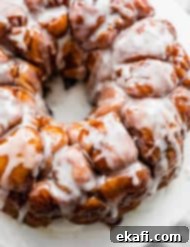 Μάνκι Μπρεντ 11 Η καλύτερη συνταγή Monkey Bread καλυμμένη με λευκό γλάσο σε λευκή πιατέλα.