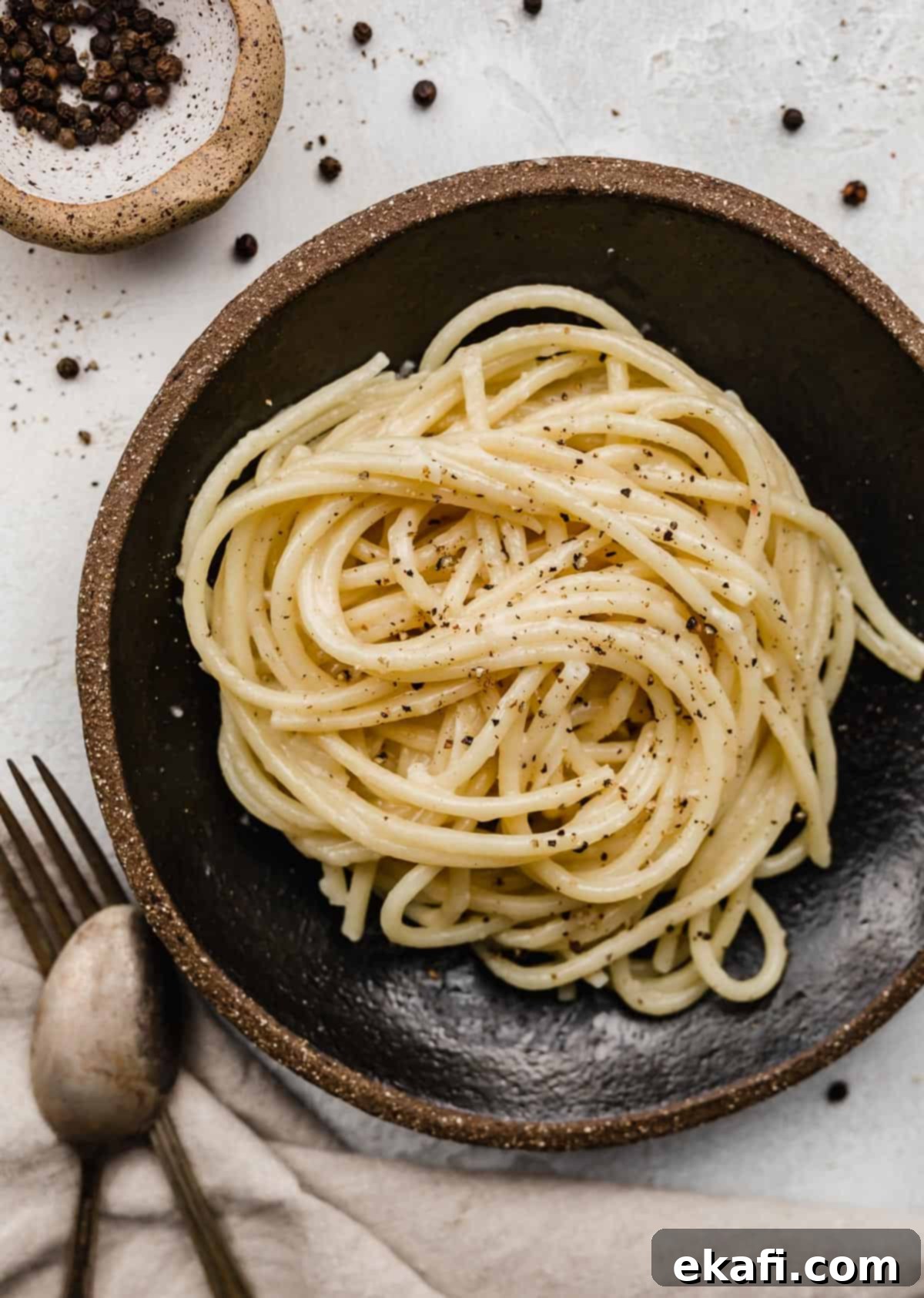 Μπουκατίνι Κάτσο ε Πέπε 2 Bucatini Cacio e Pepe noodles swirled in a black bowl.