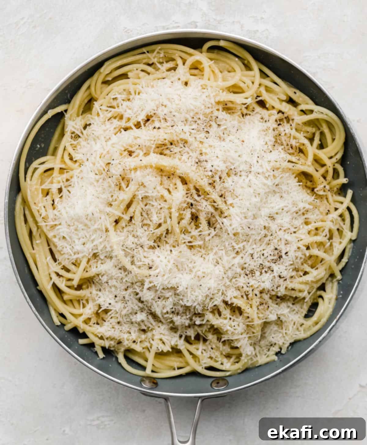 Μπουκατίνι Κάτσο ε Πέπε 4 A gray skillet full of bucatini noodles topped with fresh parmesan cheese.