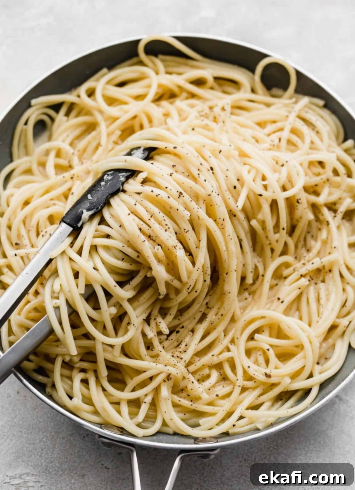 Μπουκατίνι Κάτσο ε Πέπε 5 Kitchen tongs turning Bucatini Cacio e Pepe noodles in a skillet.