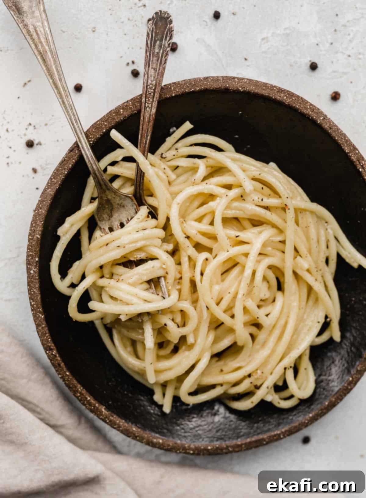 Μπουκατίνι Κάτσο ε Πέπε 6 A black plate with two forks twirled into Bucatini Cacio e Pepe noodles.