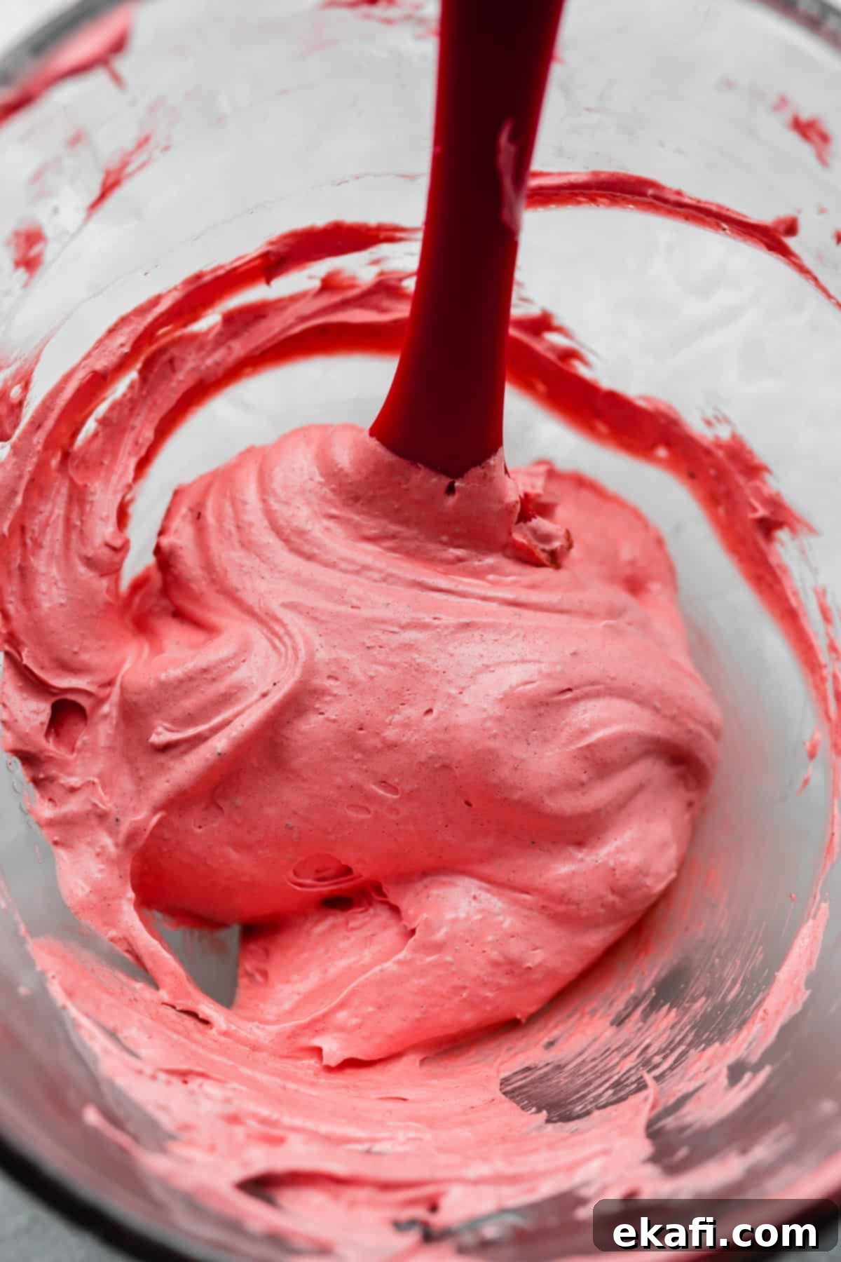 Μακαρόν Κόκκινο Βελούδο 4 A red spatula stirring a dark pink colored macaron batter in a glass bowl.
