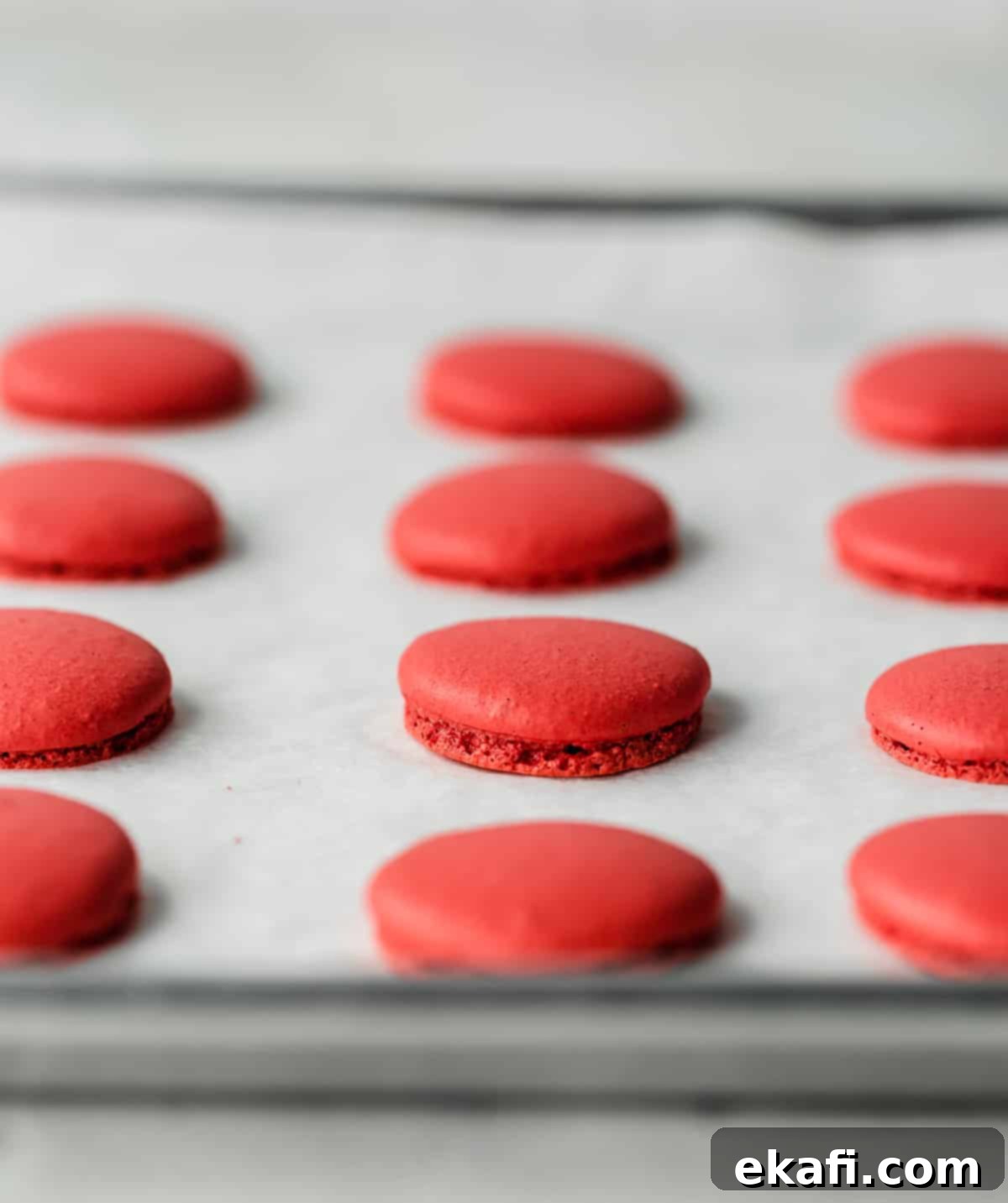 Μακαρόν Κόκκινο Βελούδο 7 Baked Red Velvet Macarons on a white parchment lined baking sheet.