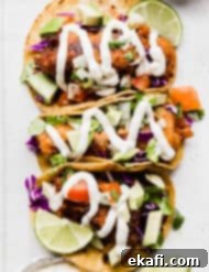 Crispy Fish Taco Bliss 12 Authentic Baja Fish Tacos topped with white sauce, cabbage, and tomatoes, on a white plate, ready to be served.