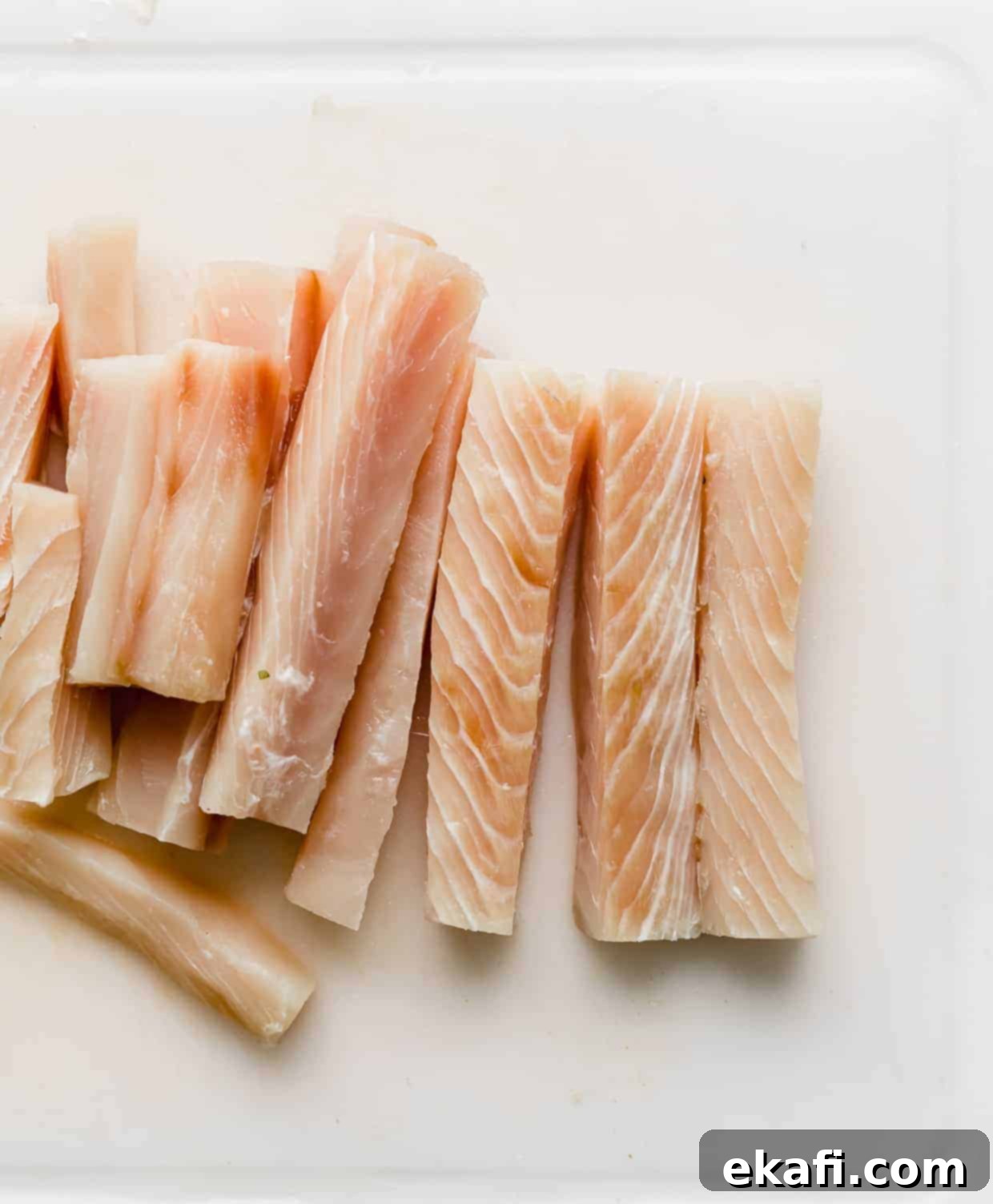 Crispy Fish Taco Bliss 6 Mahi Mahi fish sliced into uniform thin strips resting on a white cutting board, perfectly prepped for battering.