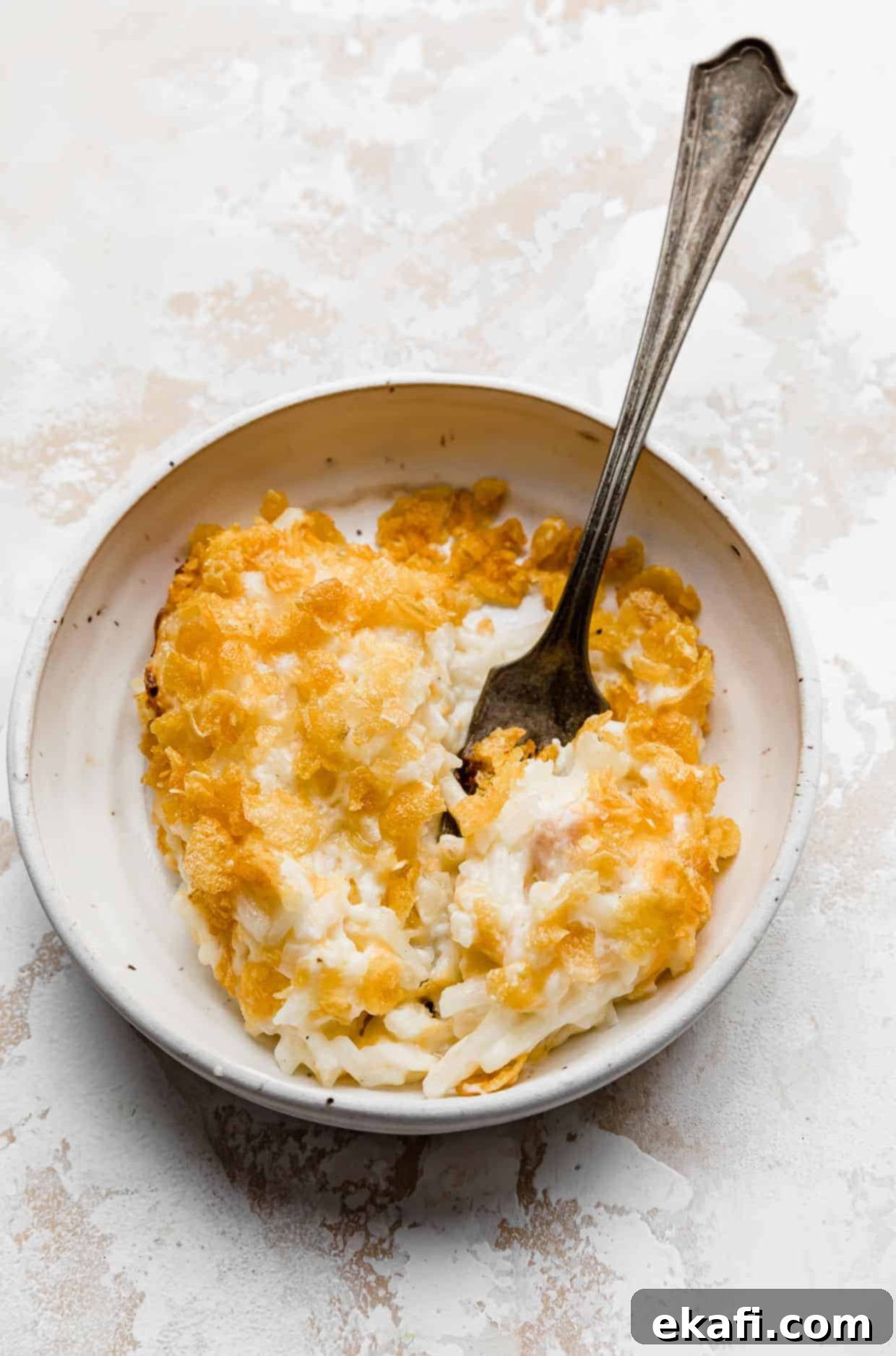 Soul-Soothing Spuds 2 A serving of golden-brown funeral potatoes on a white plate with a fork, against a white background.