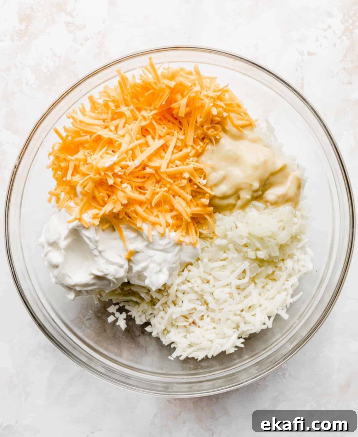 Soul-Soothing Spuds 4 A large bowl filled with shredded hashbrowns, cheddar cheese, sour cream, and cream of chicken soup before mixing.