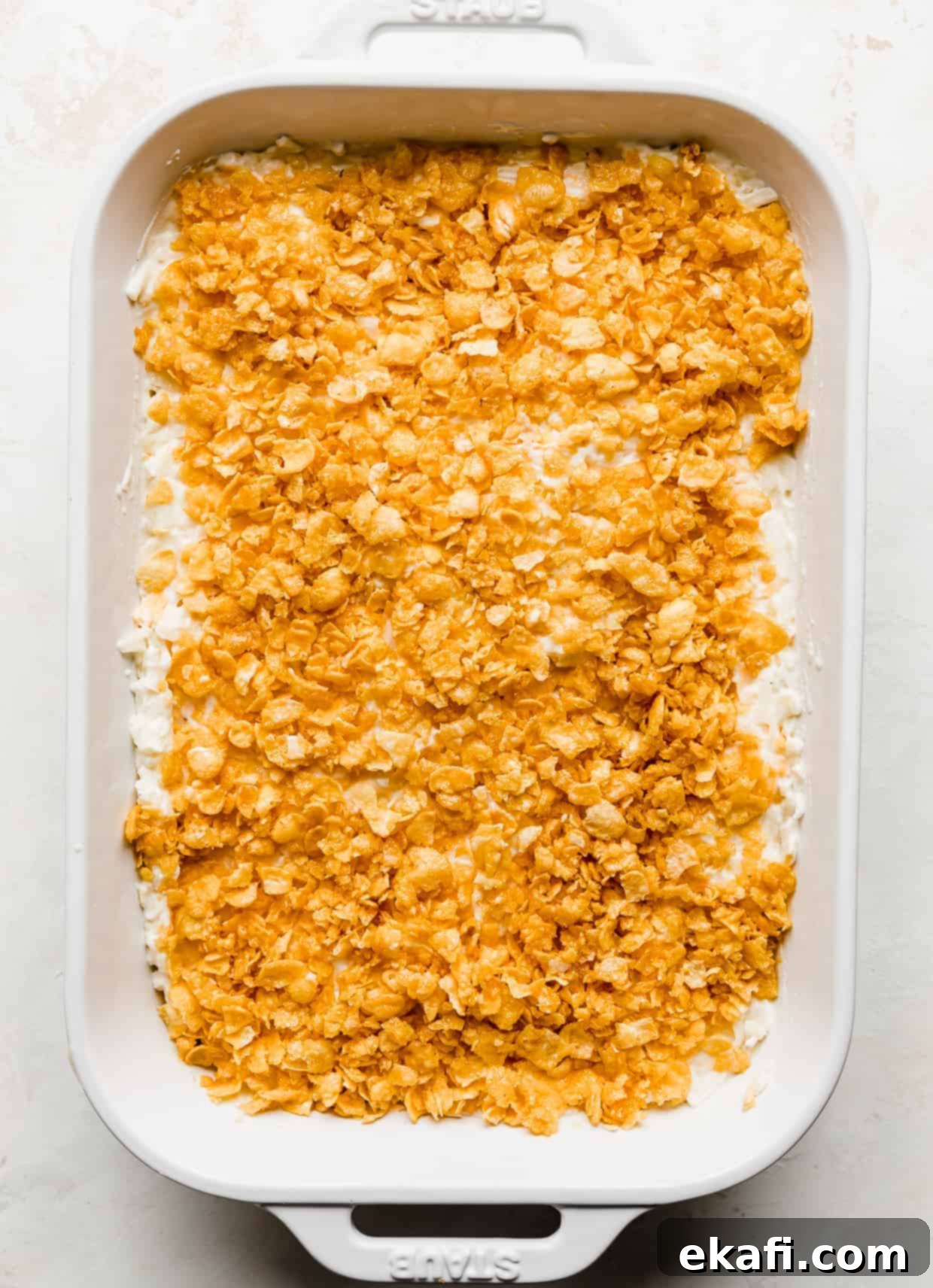Soul-Soothing Spuds 8 A casserole dish full of unbaked funeral potatoes topped with crushed cornflakes, ready to bake, against a white background.