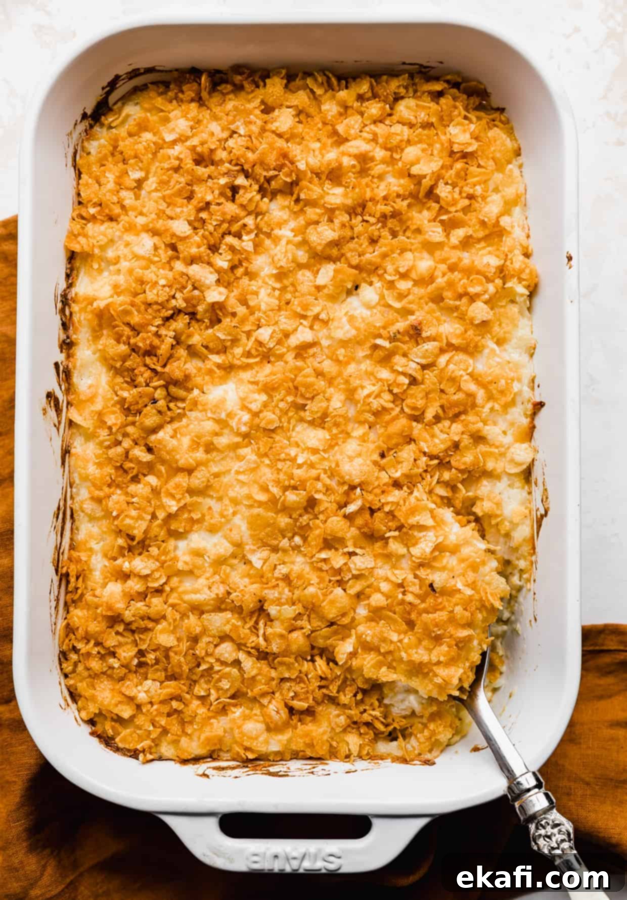 Soul-Soothing Spuds 9 Baked funeral potatoes topped with golden orange cornflakes, with a serving spoon scooping up a helping of potatoes from the dish.