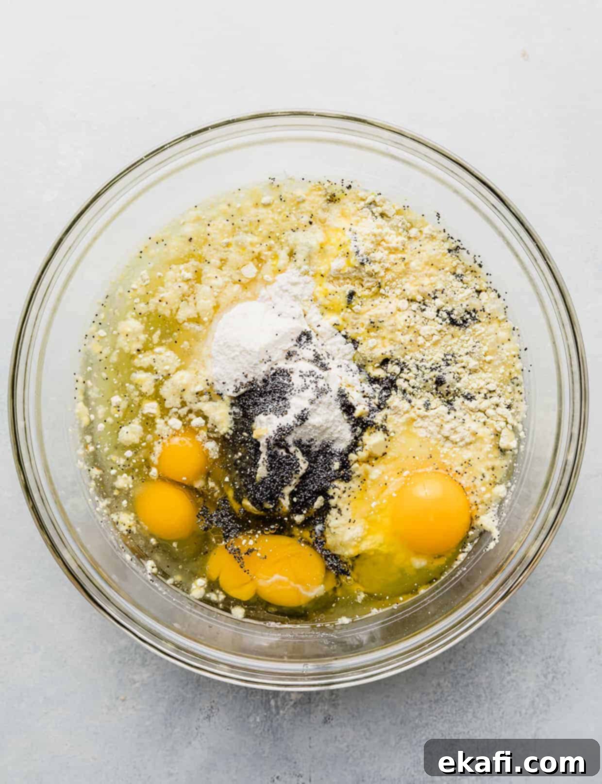 Cake Mix Lemon Poppy Seed Loaf 4 A glass bowl full of dry lemon cake mix, water, oil, 4 cracked eggs, lemon pudding mix, and poppy seeds.