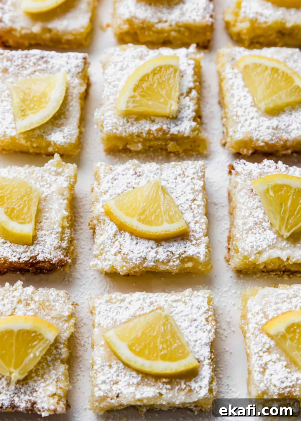 Irresistible Old Fashioned Lemon Squares 2 Lemon bars topped with powdered sugar and a wedge of fresh lemon, ready to be served.