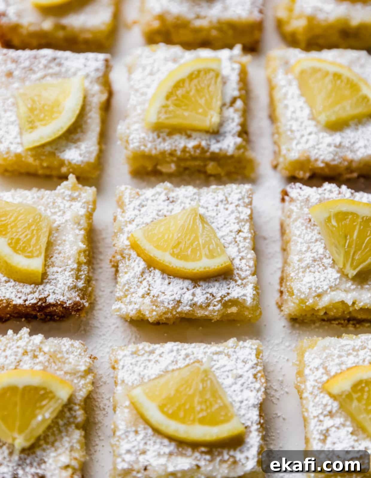 Irresistible Old Fashioned Lemon Squares 11 Beautifully arranged lemon bars, each topped with powdered sugar and a fresh slice of lemon, showcasing their vibrant color and texture.