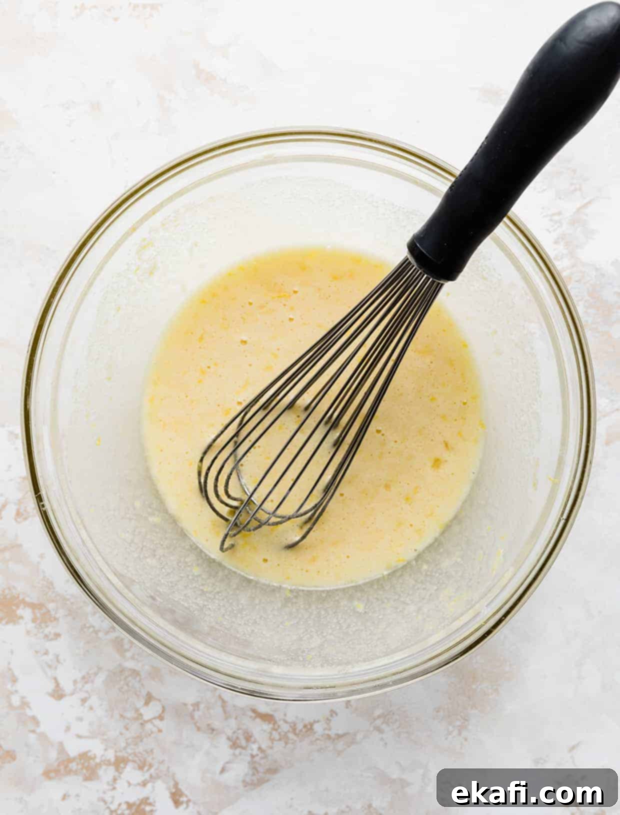 Irresistible Old Fashioned Lemon Squares 5 A glass bowl containing a vibrant yellow lemon bars filling, with a whisk resting inside.