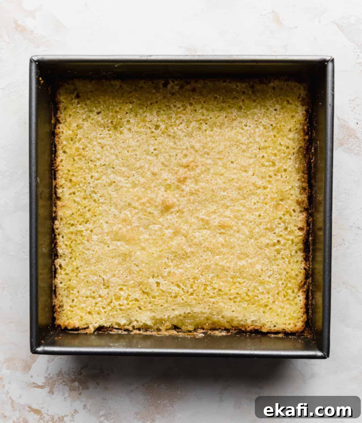 Irresistible Old Fashioned Lemon Squares 7 A square pan filled with perfectly baked yellow lemon bars, against a light-colored background.