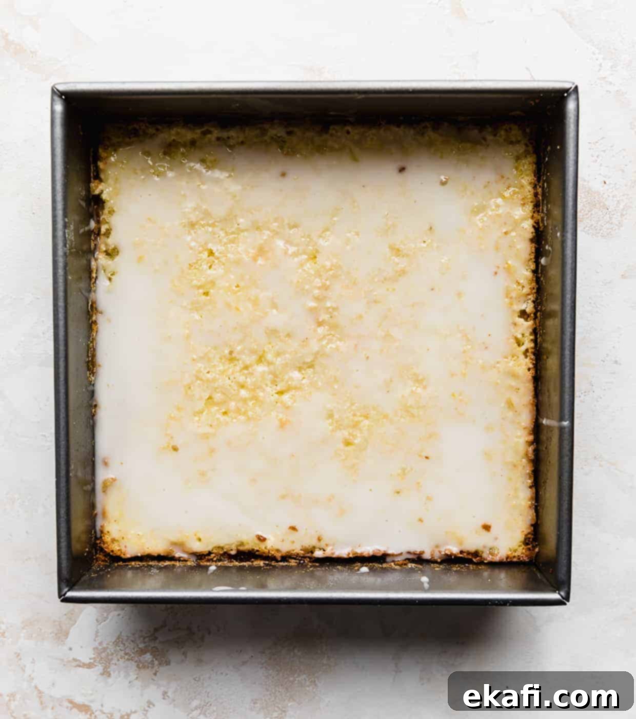 Irresistible Old Fashioned Lemon Squares 8 A square pan against a white background with glazed lemon bars, showing the optional drizzle.