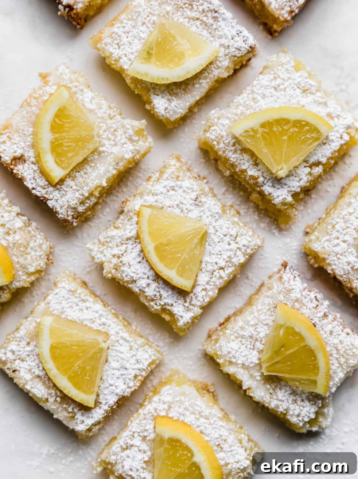 Irresistible Old Fashioned Lemon Squares 10 Overhead photo of perfectly cut lemon bars against a white background, garnished with fresh lemon wedges and powdered sugar.
