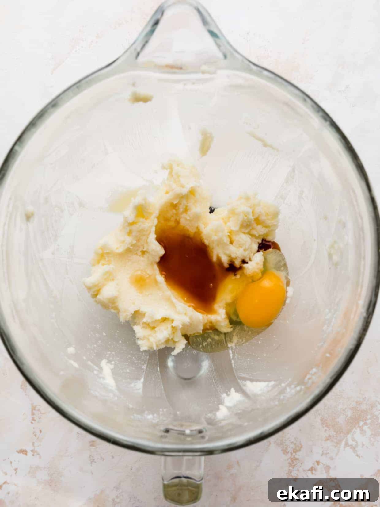 Magic Lucky Charms Cookies 4 A glass bowl with creamed butter and sugar, vanilla extract, and a cracked egg in it, against a white background.