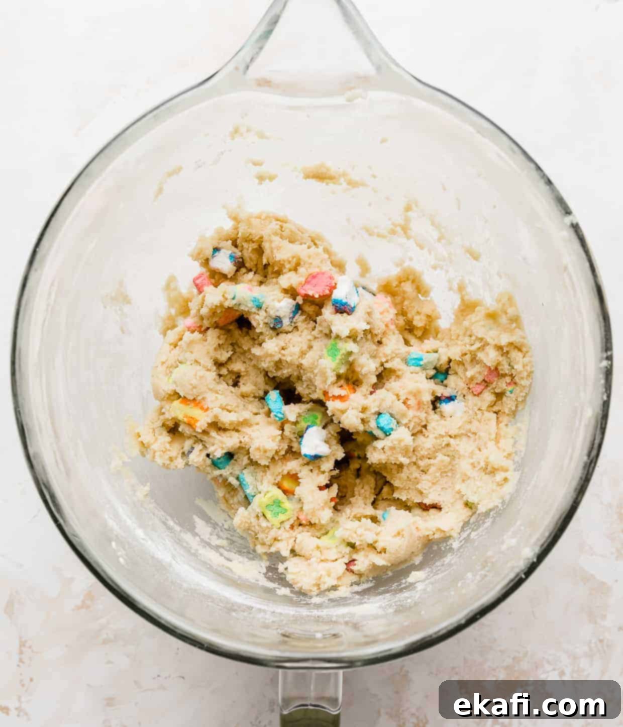 Magic Lucky Charms Cookies 9 Lucky Charms marshmallows mixed into sugar cookie dough in a glass bowl, creating a vibrant mixture.