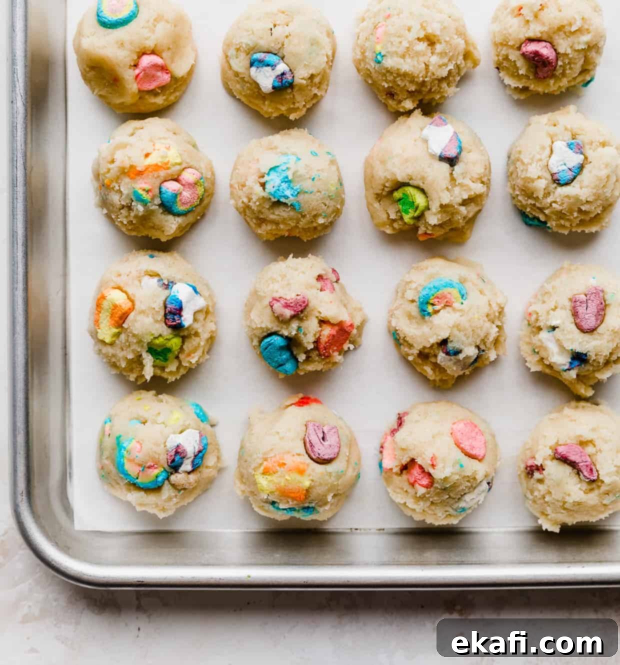 Magic Lucky Charms Cookies 10 A white parchment-lined baking sheet with balls of sugar cookie dough, each topped with a few Lucky Charms marshmallows.