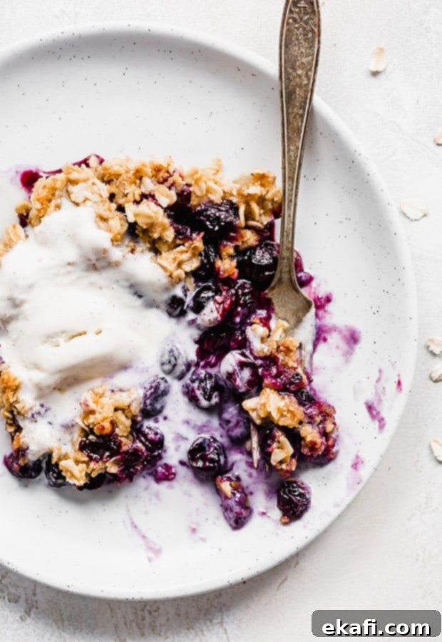 Τραγανό γλυκό μύρτιλο 2 Blueberry crisp σε πιάτο, με μια μπάλα παγωτό βανίλια από πάνω.