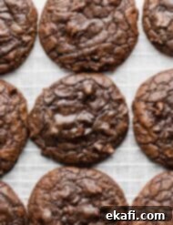 Fudgy Brownie Cookies 11 Overhead photo of a batch of freshly baked Brownie Mix Cookies on white parchment paper, highlighting their crackly tops.