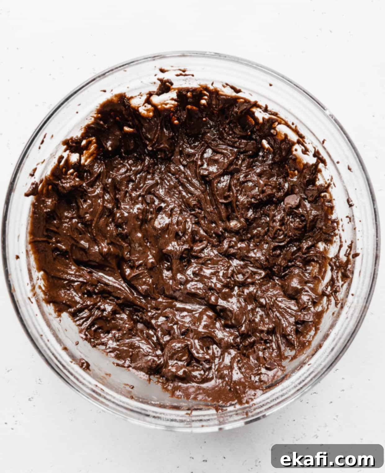 Fudgy Brownie Cookies 5 A glass bowl full of rich brownie cookie batter studded with glossy chocolate chips, showing a perfectly mixed consistency.
