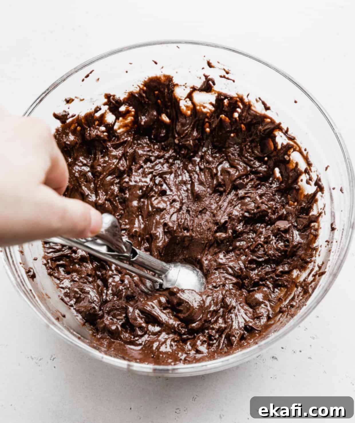 Fudgy Brownie Cookies 6 A hand holding a cookie scoop reaching into a bowl full of soft, dark Brownie Mix Cookie dough batter, ready for portioning.