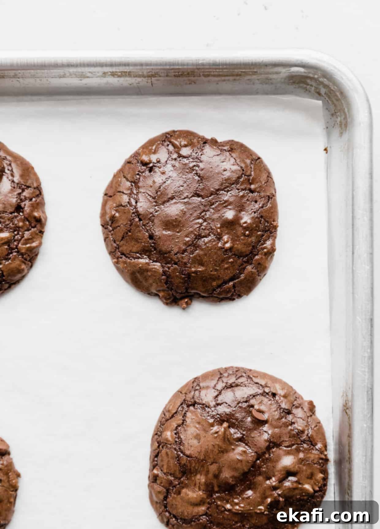 Fudgy Brownie Cookies 7 A freshly baked Brownie mix cookie with a characteristic crackly top, resting on a parchment-lined baking sheet against a white background.