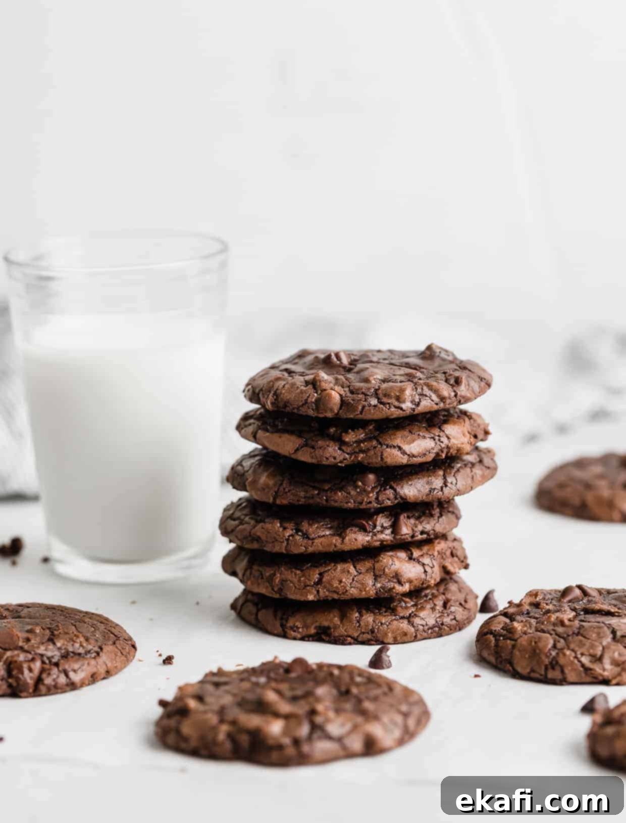 Fudgy Brownie Cookies 9 A stack of dark brown brownie cookies with a tall glass of milk next to it against a crisp white background, perfect for a treat.