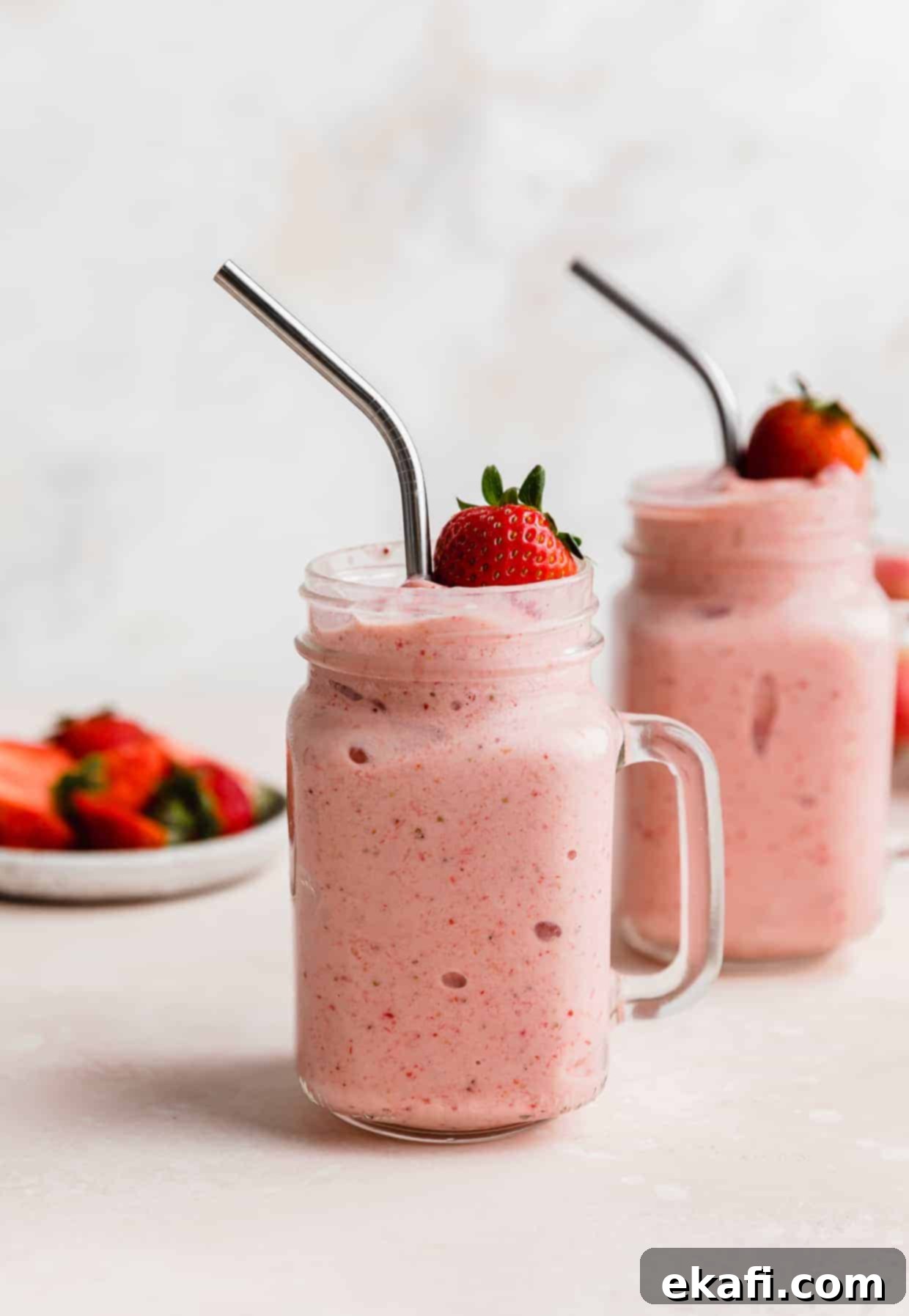 Tropical Strawberry Pineapple Smoothie 2 Two mason jar glasses full of Strawberry Pineapple Smoothie with a fresh strawberry resting on the top of the smoothie.