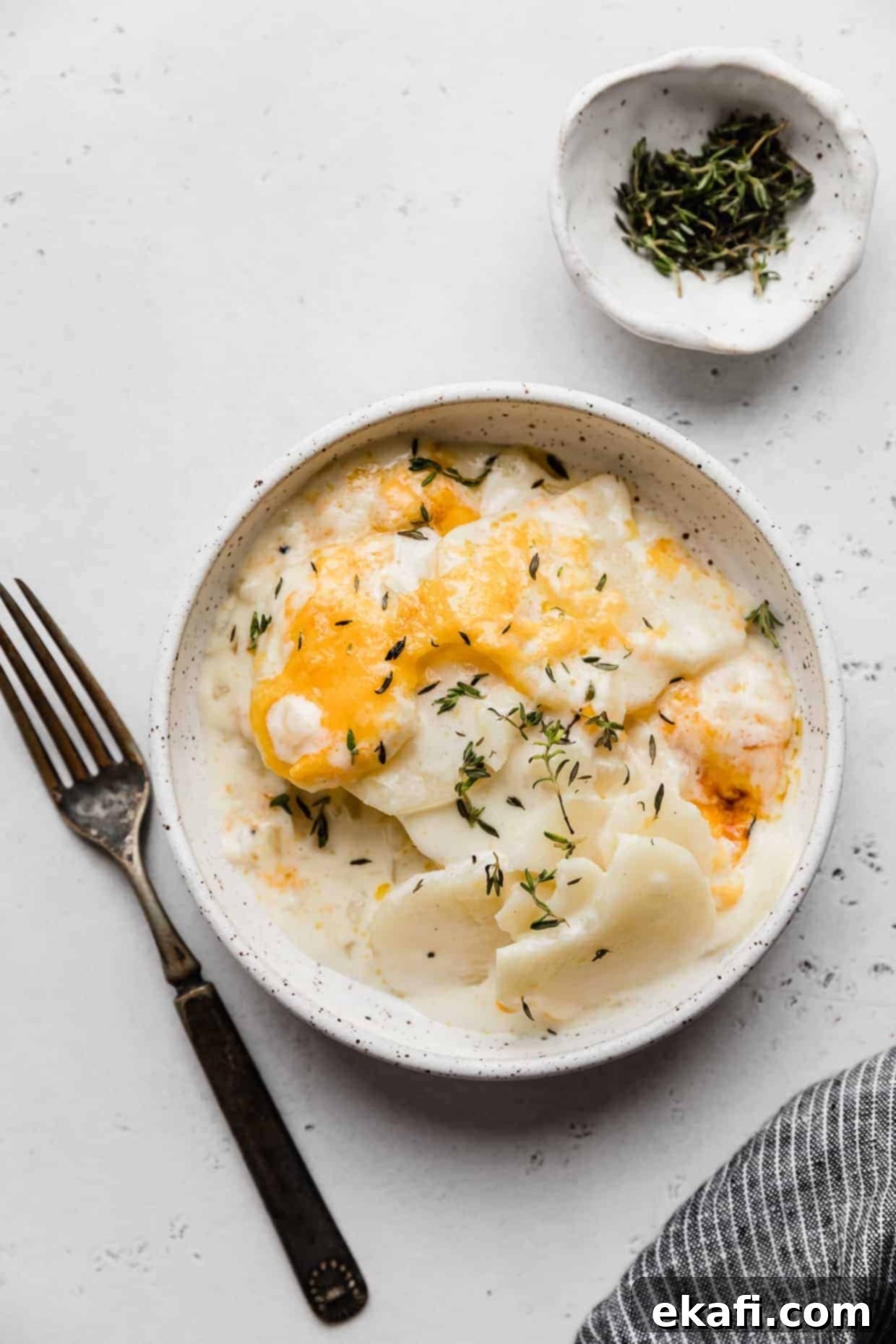 Creamy Gluten-Free Scalloped Potatoes 2 A white plate with scalloped potatoes in a creamy sauce topped with melted cheddar cheese and fresh thyme.