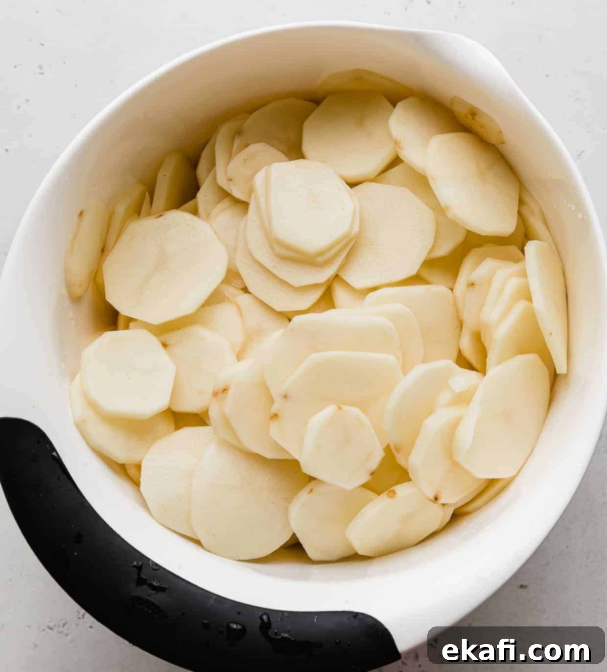 Creamy Gluten-Free Scalloped Potatoes 4 A white bowl full of raw thinly sliced potatoes.