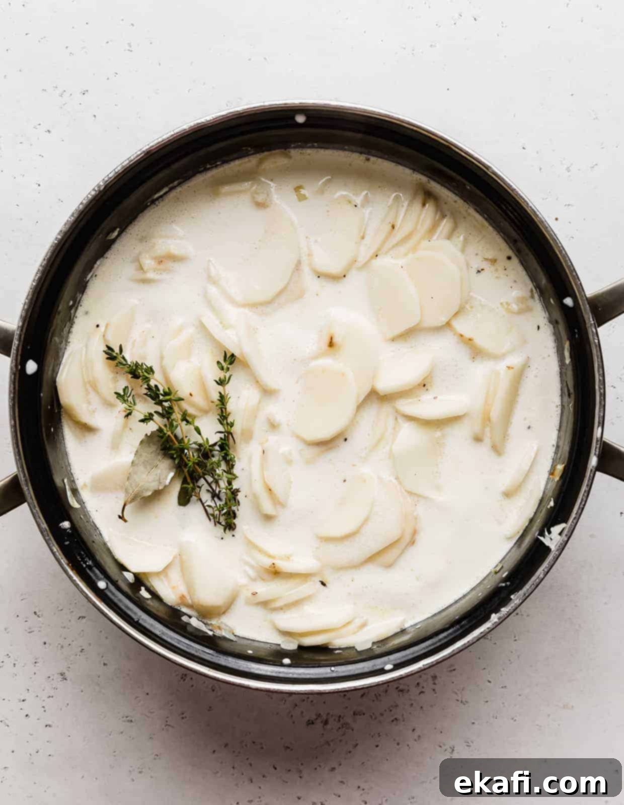 Creamy Gluten-Free Scalloped Potatoes 5 A large black pot full of heavy cream, thinly sliced potatoes, sprigs of thyme, and bay leaves.