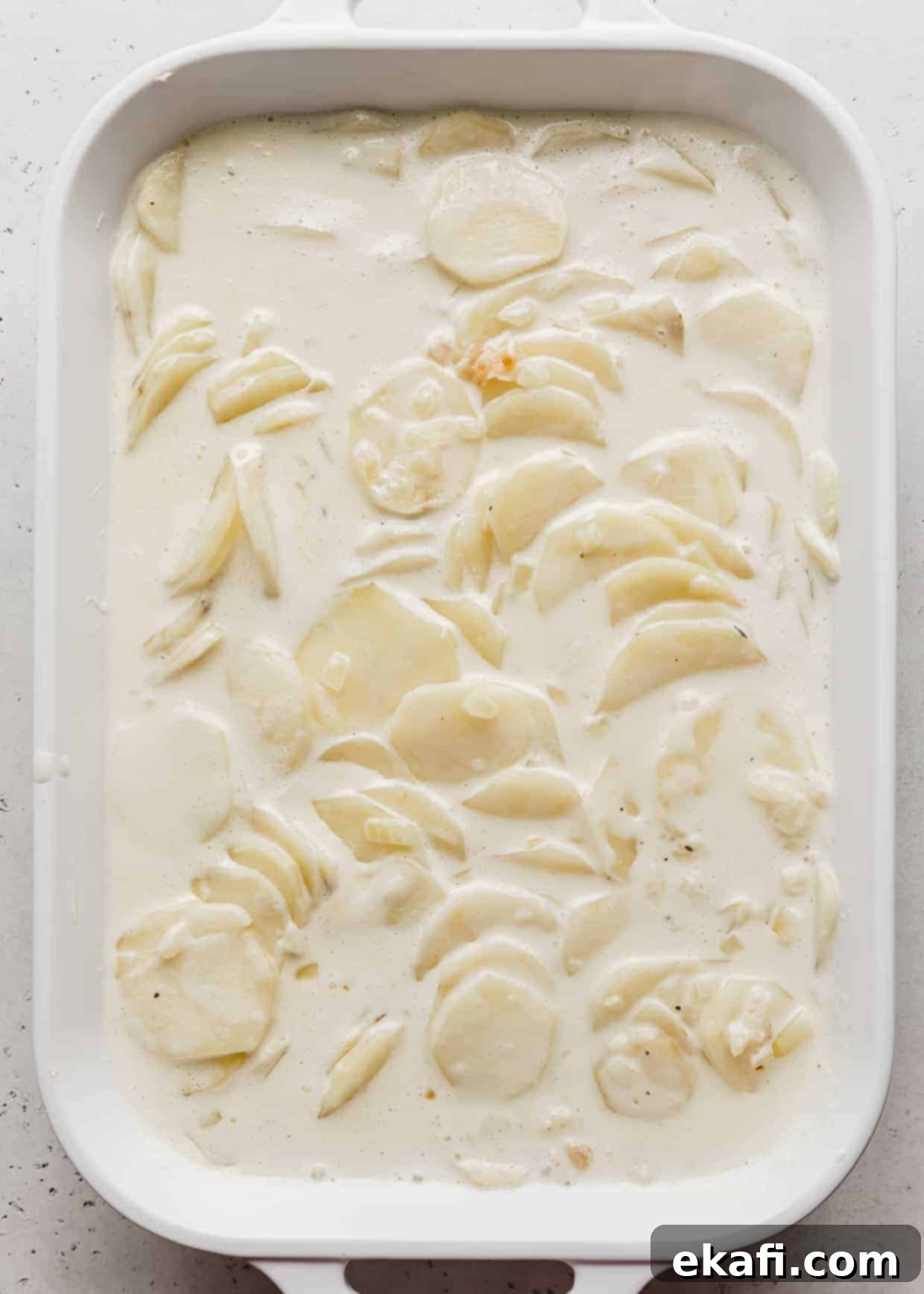 Creamy Gluten-Free Scalloped Potatoes 6 A white casserole dish full of thinly sliced potatoes loaded with heavy cream.