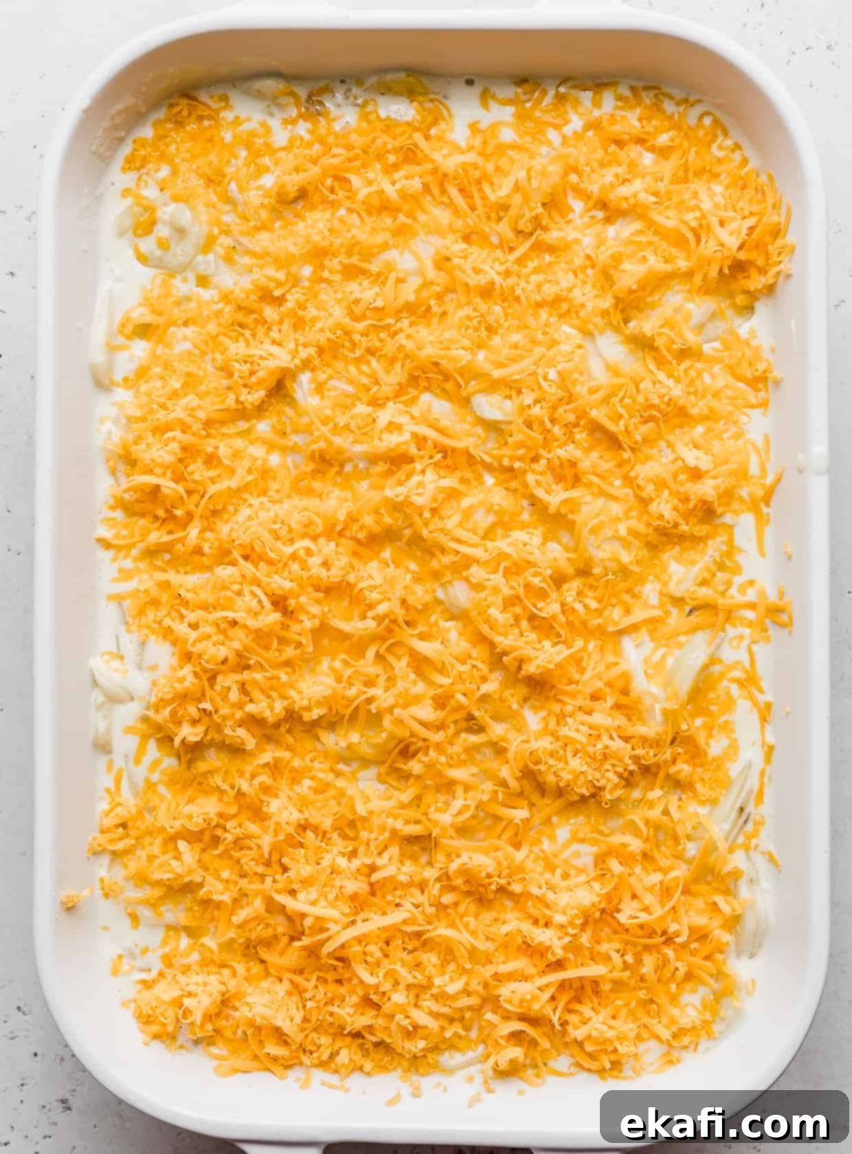 Creamy Gluten-Free Scalloped Potatoes 7 A white casserole dish topped with shredded cheddar cheese.