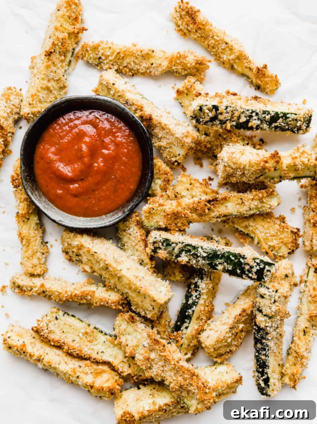Crispy Baked Zucchini Fries 7 Zucchini fries on a white background with a small bowl of marinara sauce next to the fries.