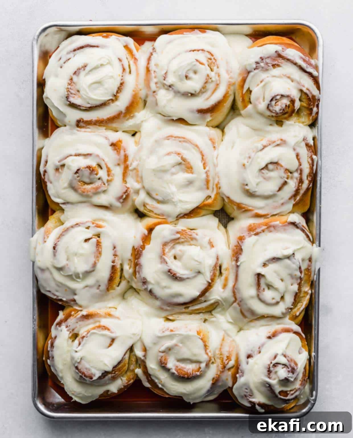Orange Rolls 11 Twelve large orange rolls on a baking sheet with thick white orange-infused frosting generously spread over each roll, ready to be enjoyed.