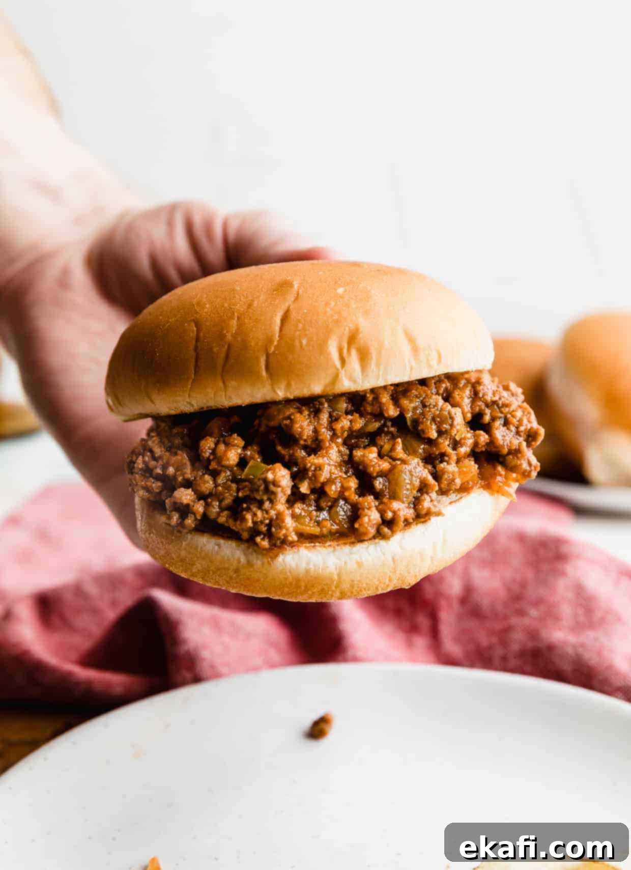 Hearty Old School Sloppy Joes 2 A hand holding up a hamburger bun that is very full of the best homemade sloppy Joe mix, showcasing the rich, saucy meat and perfectly toasted bun.
